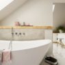 White bathtub next to a shelf with candles in monochromatic bathroom in the attic