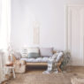 Blanket and pillows on wooden sofa in white loft interior with pouf and plant on carpet. Real photo