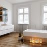 Group of burning candles on the wooden floor alongside the bathtub in a spacious bright white bathroom with large windows and wall-mounted vanities, 3d render